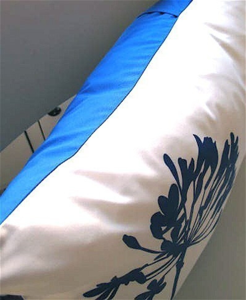 May include: A white pillow with a blue border and a blue floral design. The pillow is made of a soft, smooth fabric.