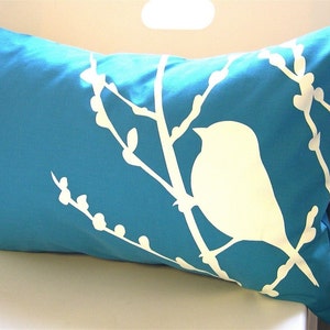 May include: A turquoise blue pillow with a white silhouette of a bird on a branch with buds.