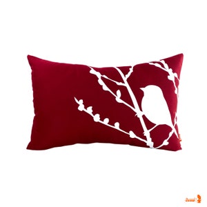May include: A red pillow with a white silhouette of a bird on a branch with buds.