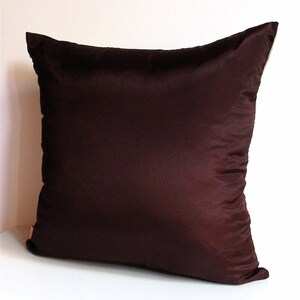 May include: A dark brown square pillow with a smooth, silky texture. The pillow is made of a soft, luxurious fabric.