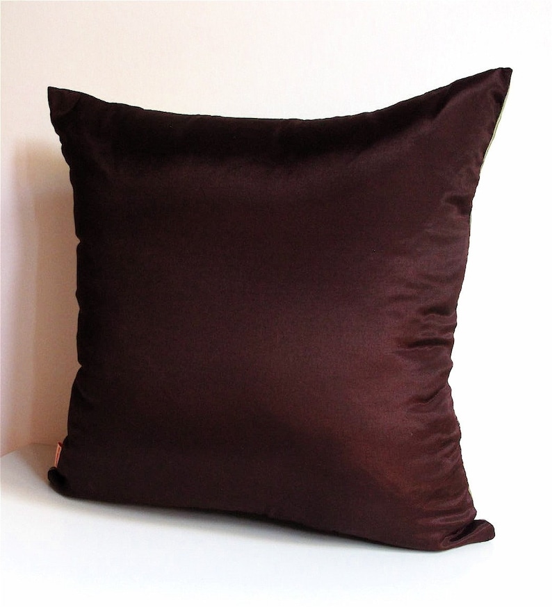 May include: A dark brown square pillow with a smooth, silky texture. The pillow is made of a soft, luxurious fabric.