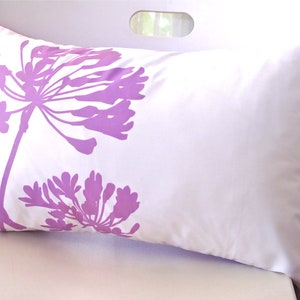 May include: White pillow with a purple floral design and a small bird silhouette. The pillow has a white background with a purple floral design and a small bird silhouette in the lower left corner. The pillow is on a white surface.
