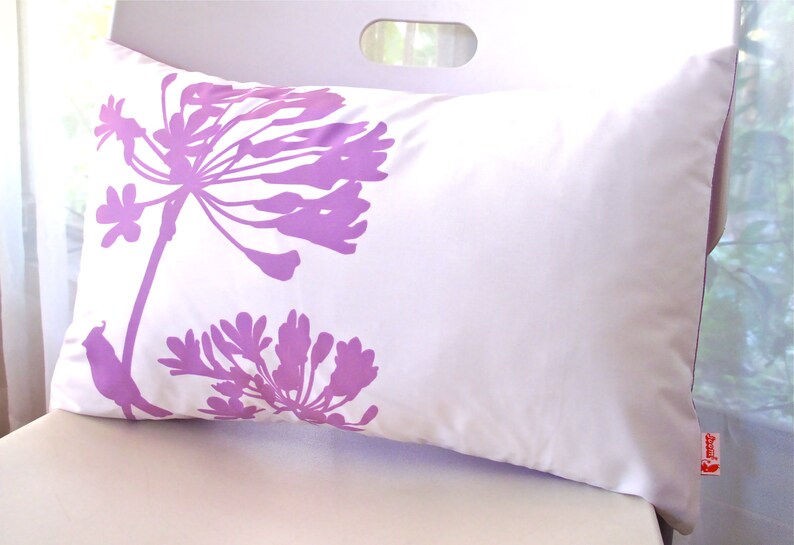 May include: White pillow with a purple floral design and a small bird silhouette. The pillow has a white background with a purple floral design and a small bird silhouette in the lower left corner. The pillow is on a white surface.