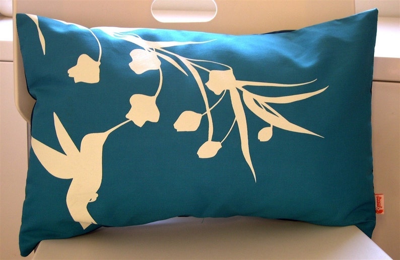 Puede incluir: Almohada azul turquesa con una silueta blanca de un colibr&iacute; y flores.