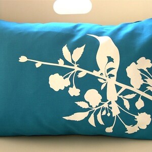 May include: A teal blue throw pillow with a white silhouette of a bird perched on a branch with flowers.