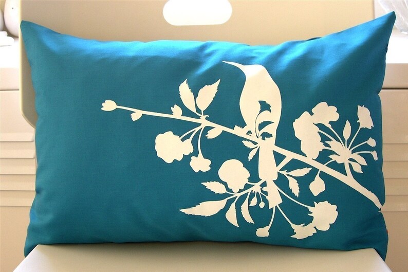 May include: A teal blue throw pillow with a white silhouette of a bird perched on a branch with flowers.