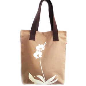 Op de afbeelding: Een bruine canvas tote bag met bruine hengsels en een wit orchidee&euml;nontwerp.