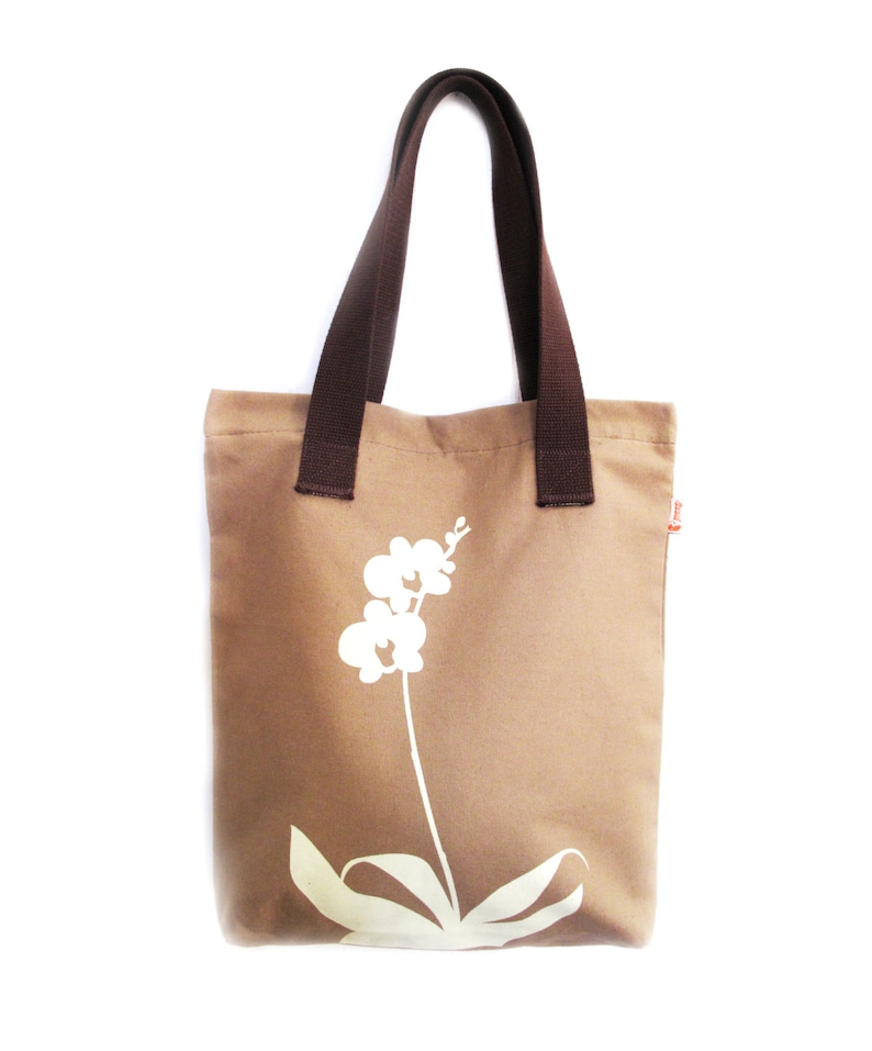 Op de afbeelding: Een bruine canvas tote bag met bruine hengsels en een wit orchidee&euml;nontwerp.
