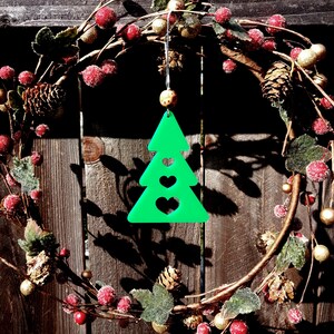 May include: A green Christmas tree ornament with three hearts cut out. The ornament is hanging from a wreath made of green leaves, red berries, and gold accents.