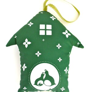 May include: A green fabric house-shaped ornament with a white window and a white silhouette of two birds and a baby bird inside a circle. The ornament has a green and white ribbon loop for hanging.