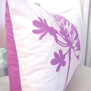 May include: A white pillow with a purple floral design. The pillow has a purple border.