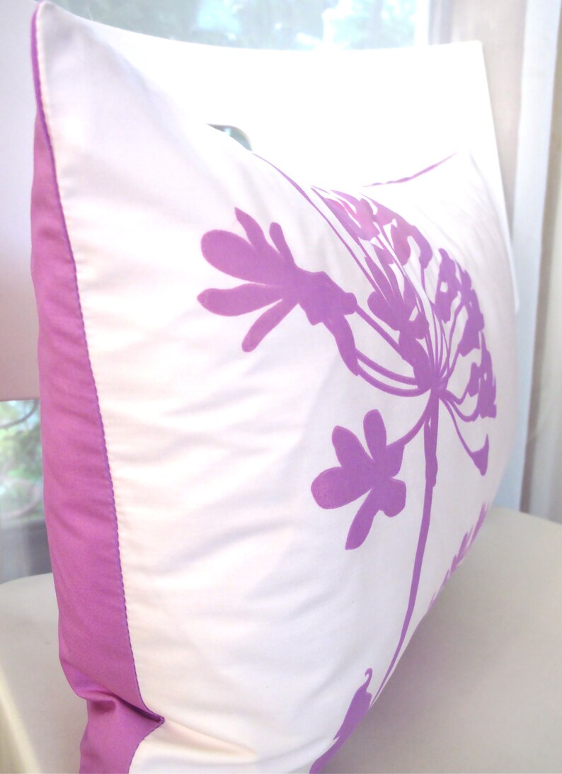 May include: A white pillow with a purple floral design. The pillow has a purple border.