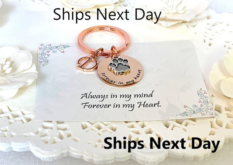 May include: Rose gold keychain with a paw print charm and a letter "D" charm. The paw print charm has the words "forever in my heart" engraved on it. The card reads "Always in my mind, Forever in my Heart."