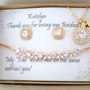 K&ouml;nnte beinhalten: Ein goldfarbenes Schmuckset, bestehend aus einer Halskette, Ohrringen und einem Armband, pr&auml;sentiert in einer Geschenkbox. Die Ohrringe und die Halskette haben quadratische, klare Edelsteine. Das Armband hat ein florales Design.