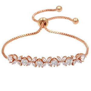 K&ouml;nnte beinhalten: Verstellbares Armband in Ros&eacute;gold mit floralem Design und klaren Kristallen. Das Armband hat eine zarte Kette und eine verschiebbare Perle zur Anpassung. Ein wundersch&ouml;nes Schmuckst&uuml;ck.