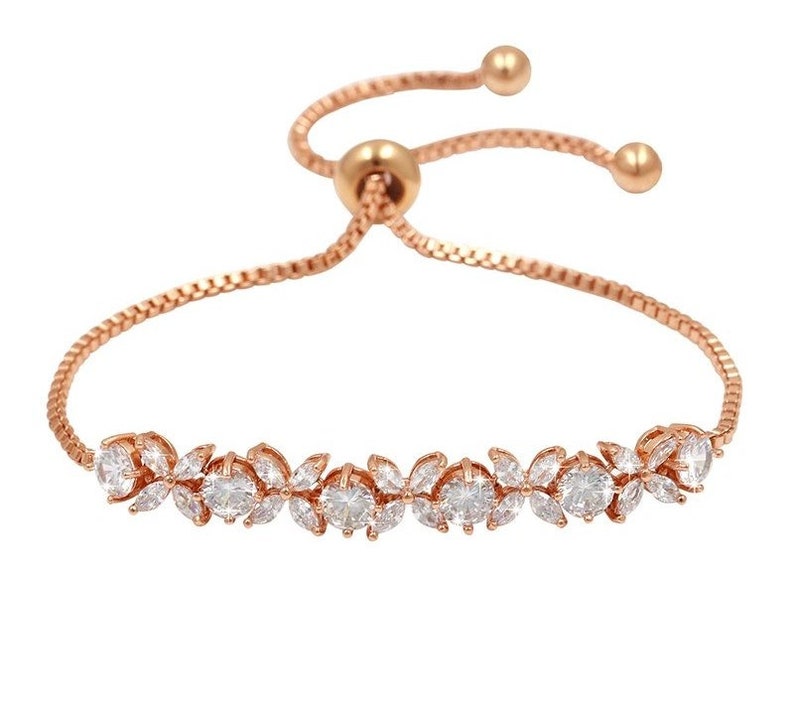 K&ouml;nnte beinhalten: Verstellbares Armband in Ros&eacute;gold mit floralem Design und klaren Kristallen. Das Armband hat eine zarte Kette und eine verschiebbare Perle zur Anpassung. Ein wundersch&ouml;nes Schmuckst&uuml;ck.