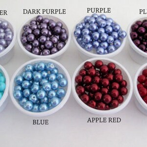 Puede incluir: Un surtido de cuentas de colores en peque&ntilde;os recipientes blancos. Los colores incluyen lavanda, morado oscuro, morado, ciruela, azul piscina, azul, rojo manzana y rojo coral. Las etiquetas de texto identifican cada color.
