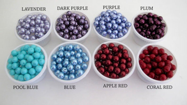 Puede incluir: Un surtido de cuentas de colores en peque&ntilde;os recipientes blancos. Los colores incluyen lavanda, morado oscuro, morado, ciruela, azul piscina, azul, rojo manzana y rojo coral. Las etiquetas de texto identifican cada color.