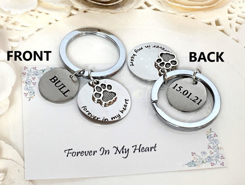 May include: A silver keychain with two round charms. One charm has a paw print and the words "forever in my heart." The other charm has the name "BULL." The back of the keychain has a charm with the date "15.01.21."