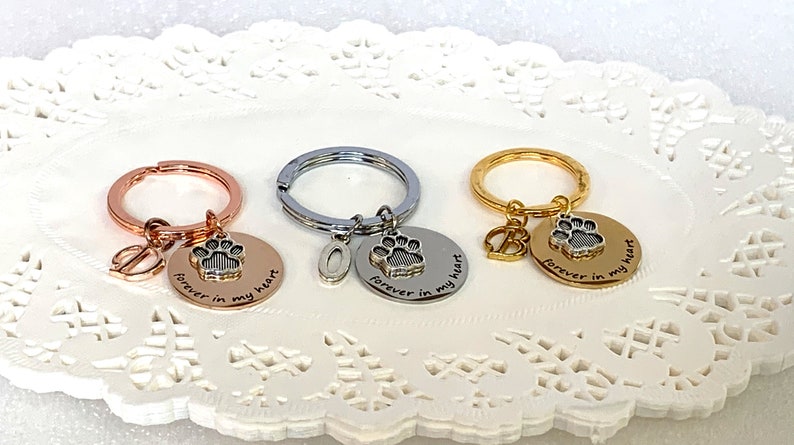 May include: Three keychains with round pendants and paw print charms. One is rose gold, one silver, and one gold. Each pendant says "forever in my heart". The rose gold keychain has a leaf charm, the silver has an "O", and the gold has a "B".