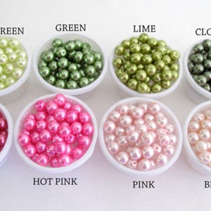 Puede incluir: Una variedad de cuentas de perlas de imitaci&oacute;n de colores en peque&ntilde;os recipientes blancos. Los colores incluyen verde claro, verde, lima, tr&eacute;bol, begonia, rosa intenso, rosa y rosa p&aacute;lido. Etiquetas de texto identifican cada color.