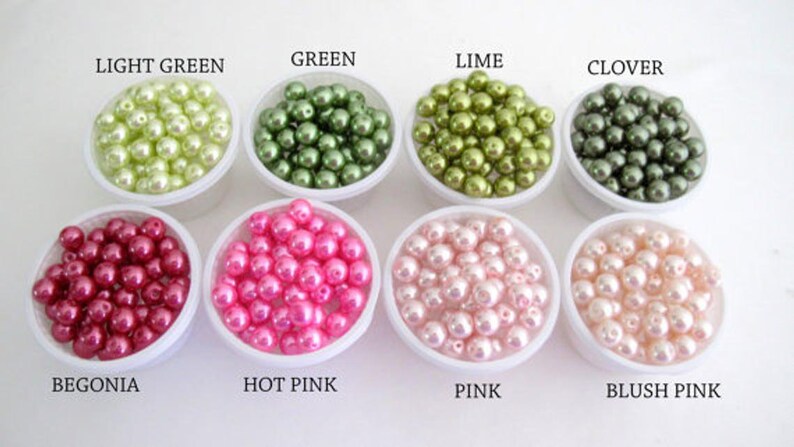 Puede incluir: Una variedad de cuentas de perlas de imitaci&oacute;n de colores en peque&ntilde;os recipientes blancos. Los colores incluyen verde claro, verde, lima, tr&eacute;bol, begonia, rosa intenso, rosa y rosa p&aacute;lido. Etiquetas de texto identifican cada color.