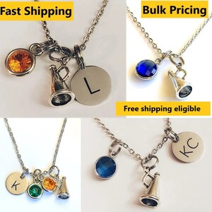May include: Silver-toned necklaces with various charms. Each necklace features a round charm with a letter, a gemstone, and a miniature megaphone charm. Gemstones are orange, blue, and green.