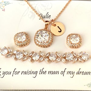 K&ouml;nnte beinhalten: Ros&eacute;goldenes Schmuckset mit einer Halskette mit Anh&auml;nger und Initialen-Charm, passenden quadratischen Ohrringen und einem floralen Armband. Das Set verf&uuml;gt &uuml;ber klare, funkelnde Steine. Die Karte lautet: "Danke, dass du den Mann meiner Tr&auml;ume gro&szlig;gezogen hast!"