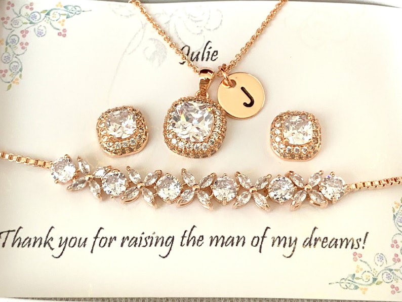 K&ouml;nnte beinhalten: Ros&eacute;goldenes Schmuckset mit einer Halskette mit Anh&auml;nger und Initialen-Charm, passenden quadratischen Ohrringen und einem floralen Armband. Das Set verf&uuml;gt &uuml;ber klare, funkelnde Steine. Die Karte lautet: "Danke, dass du den Mann meiner Tr&auml;ume gro&szlig;gezogen hast!"