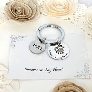 May include: Silver keychain with two round charms. One charm has the name "BULL" engraved, the other has a paw print and the words "forever in my heart". The keychain is on a card that says "Forever In My Heart".