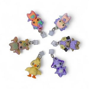 Puede incluir: Colección de seis pendientes coloridos y caprichosos. Cada pendiente presenta un diseño de animal único, incluyendo un búho, una oveja, un pollito y una criatura moteada. Los pendientes son en tonos de morado, amarillo, naranja y verde, con herrajes plateados.