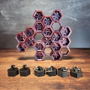 May include: A hexagonal wooden display stand with a red and purple wood grain pattern. The stand has 12 compartments and is designed to hold small items. Eight black keychains with metal rings are in the foreground.