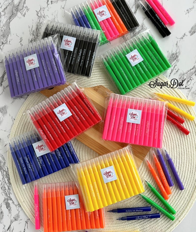 May include: A collection of colorful edible ink markers in various shades, including purple, black, green, pink, red, blue, orange, and yellow. Each set is packaged in clear plastic and features a label with the text "Sugar Dot" and "Edible Ink Marker".