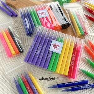 May include: Assortment of colorful edible ink markers in clear plastic packaging. The markers are in various colors, including purple, green, yellow, and pink. Each marker is labeled with "Sugar Dot" and "Edible Ink Marker".