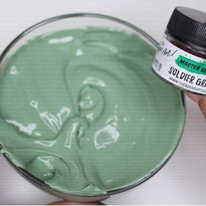 Peut inclure: Un bol en verre transparent rempli d'une substance lisse et vert clair. Un petit pot &eacute;tiquet&eacute; "MASTER ELITE SOLDIER GREEN" est tenu &agrave; proximit&eacute;. Le pot a un couvercle noir et une &eacute;tiquette blanche avec des accents verts.