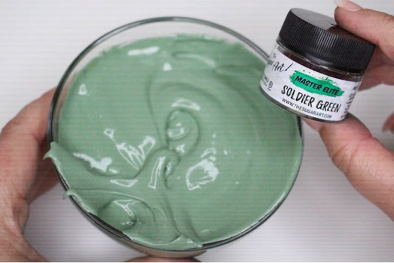Peut inclure: Un bol en verre transparent rempli d'une substance lisse et vert clair. Un petit pot &eacute;tiquet&eacute; "MASTER ELITE SOLDIER GREEN" est tenu &agrave; proximit&eacute;. Le pot a un couvercle noir et une &eacute;tiquette blanche avec des accents verts.