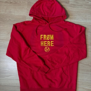 May include: A red hoodie with the words "FROM HERE" embroidered in yellow, and a stylized "V" symbol. The sweatshirt features a front pocket and a drawstring hood.