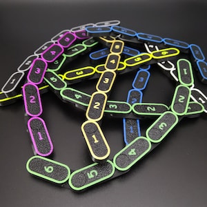 Könnte beinhalten: Ineinandergreifende schwarze Kunststoff-Zahlkacheln mit farbigen Rändern und den Zahlen 1-6. Die Kacheln sind in einem komplexen, miteinander verbundenen Muster vor einem dunklen Hintergrund angeordnet. Die Ränder sind in verschiedenen Farben, darunter Pink, Gelb, Grün und Blau.