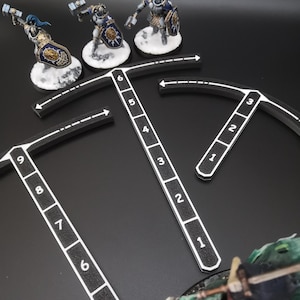 Op de afbeelding: Miniatuurfiguren van gepantserde krijgers met hamers en schilden, op besneeuwde bases, zijn gepositioneerd in de buurt van zwart-witte meetgereedschappen. De gereedschappen hebben genummerde markeringen en de scène speelt zich af tegen een donkere achtergrond, wat wijst op een tabletopspel.