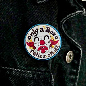 May include: A round button with a cartoon clown face and the text "only a Bozo relies on air." The clown has red hair, a red nose, and a sad expression. The button has a blue border and is on a black denim jacket.