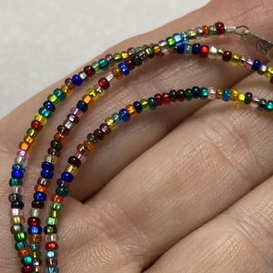 May include: A multi-strand necklace made with tiny colorful glass beads. The necklace is layered and features a silver clasp.