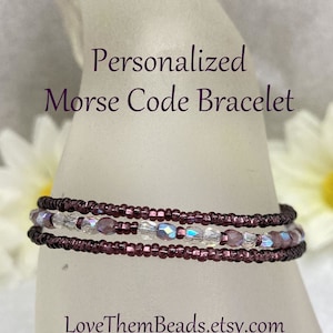 May include: A personalized Morse code bracelet made with purple and clear beads. The bracelet is on a white mannequin hand. The text "Personalized Morse Code Bracelet" and "LoveThemBeads.etsy.com" are visible in the image.