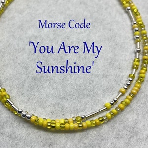 May include: A yellow and silver beaded bracelet with the message "You Are My Sunshine" in Morse code.