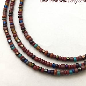 May include: A multi-strand necklace made with small brown, blue, and gold beads. The necklace is layered and has a silver clasp.