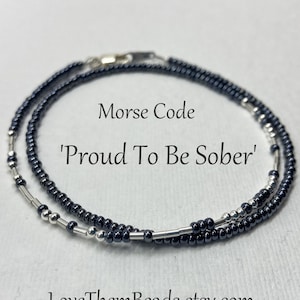May include: A black and silver beaded bracelet with the message 'Proud To Be Sober' in Morse code.