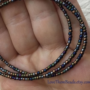 May include: A multi-strand necklace made with small iridescent beads in shades of copper, black, and silver. The necklace has a silver clasp.