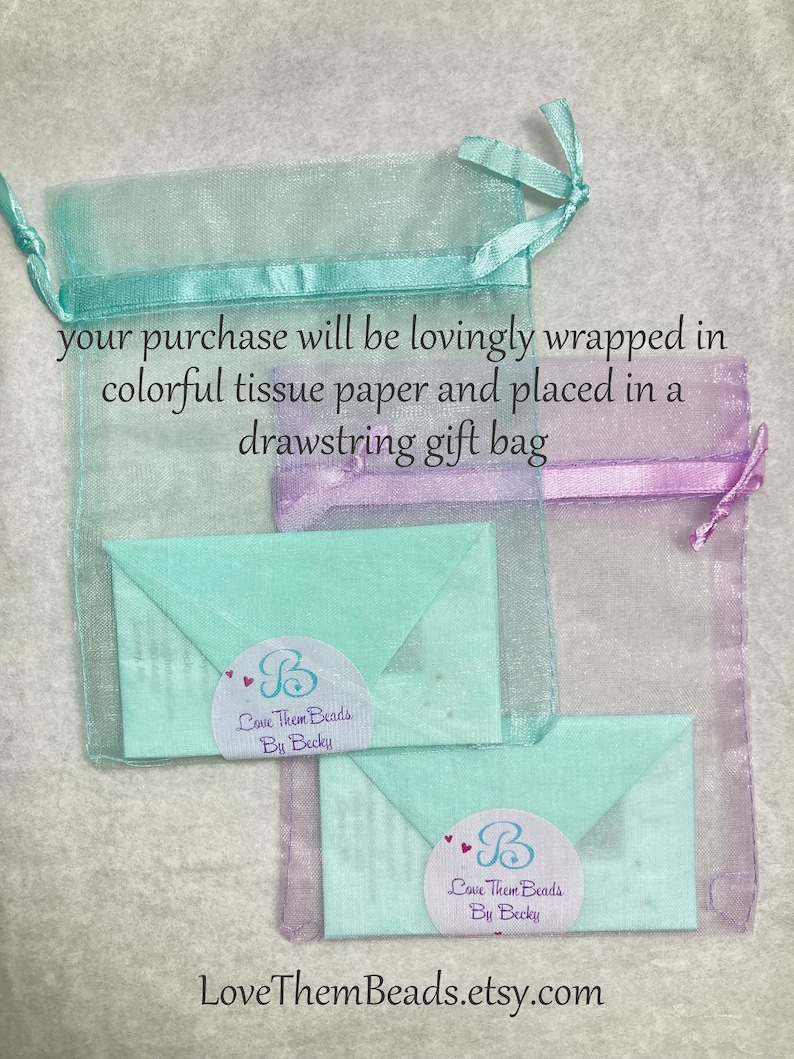 May include: A light blue and purple drawstring gift bag with two light blue envelopes inside. The envelopes have a white circle with the text "Love Them Beads By Becky" in black text. The text "LoveThemBeads.etsy.com" is printed at the bottom of the image.