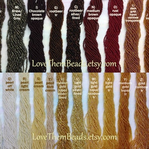 May include: A variety of seed beads in different colors and finishes, including metallic brown, brass lined grey, chocolate brown opaque, rootbeer, rootbeer silver lined, medium brown opaque, rust opaque, dark gold topaz rainbow transparent, dark gold topaz transparent, pearl white opaque, pearl off white, pearl light cream, pearl cream, pearl dark cream, medium gold topaz silver lined, light gold silver lined, light gold topaz rainbow, light gold, medium gold topaz, gold rainbow, dark gold topaz silver lined. The text "Love Them Beads.etsy.com" appears twice on the image.