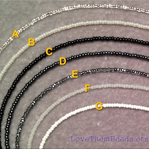 May include: Seven strands of seed beads in various colors and finishes, including silver, white, black, and gray. The beads are arranged in a semi-circle, with the largest strand at the top and the smallest strand at the bottom. The strands are labeled with letters A through G.
