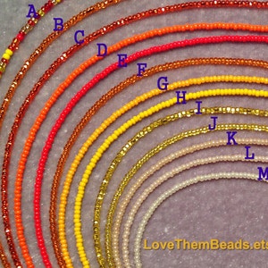 May include: A set of 13 different colored seed beads, arranged in a rainbow pattern from red to white. The beads are strung on a string and are arranged in a semi-circle. The beads are labeled with letters from A to M.